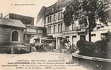 Carte postale en noir et blanc. Voitures attelées sur une place bordée de maisons et d'immeubles.