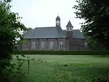 Un bâtiment de brique à toit d'ardoise, avec de hautes fenêtres.