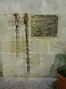 Photographie de deux chaînes pendantes d'un mur à côté d'une plaque de laiton brillant.