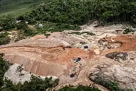 Photographie couleur aérienne d'une zone déboisée et excavée au milieu d'une forêt équatoriale.