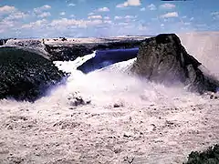 Vue de la brèche dans le barrage Teton le 5 juin 1976 : la retenue (en arrière-plan) se vide entre la paroi rocheuse (à gauche) et ce qui reste du barrage (à droite).