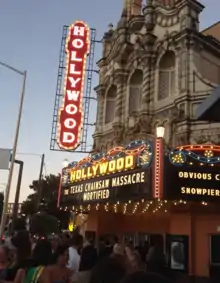 Photo d'un cinéma accueillant des spectateurs le soir. Des enseignes lumineuses indiquent le nom du film projeté : Massacre à la tronçonneuse.