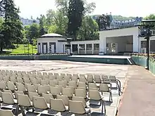 Photographie en couleurs d'une esplanade garnie de rangées de chaises au premier plan, scène au second plan.