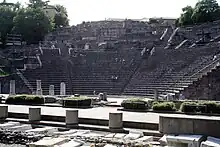 Photo des restes d'un amphithéâtre romain, avec des visiteurs assis sur les marches.