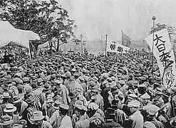 Photographie en noir et blanc d'un défilé de travailleurs portant quelques banderoles.
