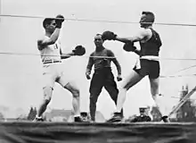 Photographie en noir et blanc de deux boxeurs s'affrontant sur un ring devant un arbitre.