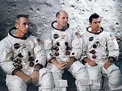 Trois hommes assis, en combinaison spatiale.