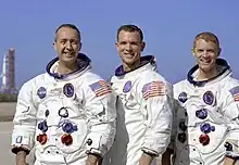 Photographie en couleur de l'équipage d'Apollo 9 en combinaison posant près du pas de tir.