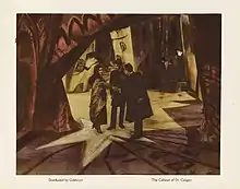 Un lobby card avec une photographie au centre, et de petites légendes en dessous. L'image représente un homme qui serre la main d'une femme, tandis qu'un autre homme les observe. Les trois personnages se tiennent au milieu d'une rue de ville, avec des murs de briques aux formes tordues et déformées, et des ombres et des traits de lumière peints sur les murs et le sol.