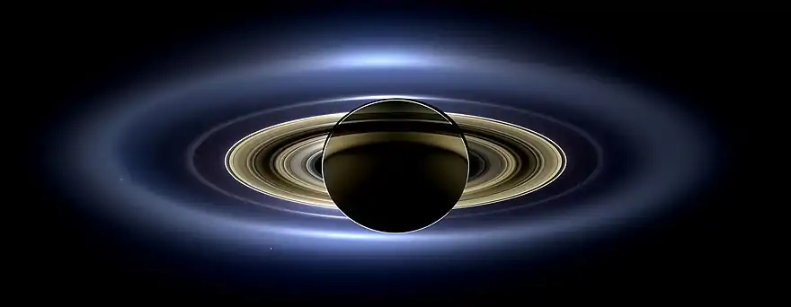Image de Saturne obscurcissant le Soleil et apparaissant de couleur orange sombre. Les anneaux les plus externes ont une couleur proche du bleu. En zoomant, de nombreuses lunes sont visibles sous forme de points blancs.