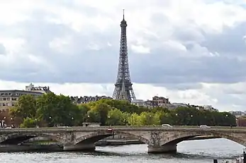 La flèche caractéristique de l'église devant le pied de la tour Eiffel.