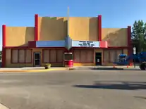 Un théâtre jaune et rouge déserté avec des fenêtres barricadées, et une grue bleue à la droite de l'image.