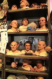 Sur des bustes posés sur une étagère sont exposés des masques en silicone avec des cheveux et des oreilles pointues.