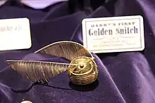 Boule d'or avec des ailes de chaque côté posées sur un rideau de velours violet
