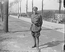 Photo en noir et blanc d'un militaire de la première guerre mondiale qui se tient au bord d'une route.