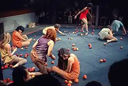 Des comédiens au sol sur scène au milieu de pommes éparpillées.