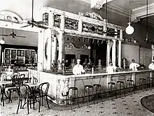Photo d'archives d'un restaurant avec un comptoir au centre et les employés posant en tenue de travail d'époque.
