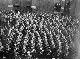 Photographie en noir et blanc de militaires en formation avec des spectateurs derrière eux