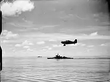 Photo en noir et blanc d'un avion à hélices survolant un navire de guerre