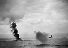 Photo en noir et blanc d'un panache de fumée sur l'eau, au milieu de navires.