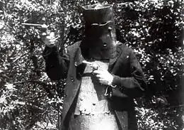 Image en noir et blanc tirée du film ; un homme casqué, portant une armure de cuir, tient un pistolet dans chaque main.