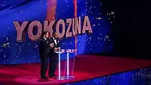 Deux hommes en smoking faisant un discours devant un pupitre.