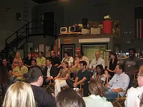 Photo prise en intérieur de plusieurs membres de l'équipe de la série assis sur des chaises et faisant face à un public.