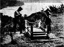 Photographie en noir et blanc de deux marins, les bras renversés, debout devant une tombe.