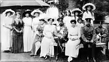 Photographie en noir et blanc montrant une quinzaine d'hommes en uniforme et de femmes vêtues de longues robes.