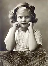 Photographie en noir et blanc d'une petite fille aux cheveux clairs appuyant son visage sur ses mains.