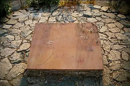 Photo en couleur d'une pierre rectangulaire déposée sur un sol en pierres et comportant une inscription en grec