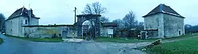 Photo panoramique d'une entrée ancienne en pierre avec une arche et entourée de deux petits bâtiments.