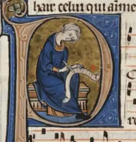 Miniature médiévale représentant un homme richement vêtu écrivant sur un long parchemin.