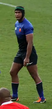 Joueur de rugby, casqué, debout, vu de côté.