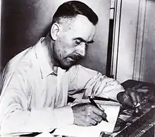 photographie en noir et blanc d'un homme d'apparence concentrée, occupé à écrire en fumant