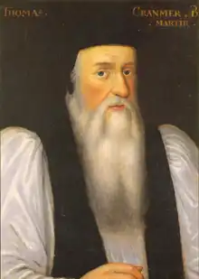 Portrait de l'archevêque Cranmer âgé. Il a un visage long avec une longue barbe blanche, un grand nez, des yeux noirs et des joues roses. Il porte des habits cléricaux sous un manteau noir avec des manches blanches et un chapeau sur la tête