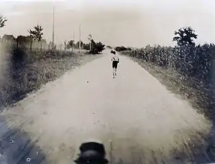 Un homme seul court au milieu d'une piste de terre, photographié depuis une voiture.