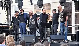 six hommes sur scène en train de saluer. Thomas de Pourquery est au milieu, chauve, longue barbe, ventru, vêtu de noir
