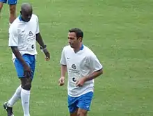Deux footballeurs en maillot blanc et short bleu.