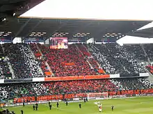 Photo montrant une tribune, avec des personnes brandissant des drapeaux blancs, rouges et noirs.