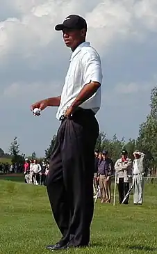 Un joueur de golf, casquette noire sur la tête, tient une balle dans sa main droite.