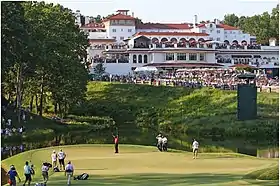 Devant une large foule réunie autour d'un green de golf, un joueur lève les bras.