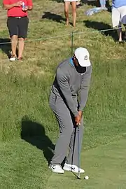 Le golfeur prépare son coup, mains jointes autour de son club au niveau de ses genoux.