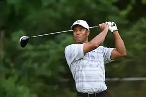 Un homme tient un club de golf dans ses mains derrière sa tête.