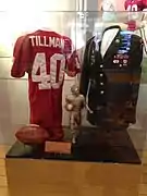 Un maillot et un ballon de football américain, un trophée et une veste militaire de Pat Tillman exposés sous une vitrine de verre.