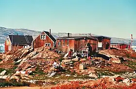 Photographie en couleurs d'un village aux maisons rouges construites sur des roches affleurantes, les rives d'un fjord visibles en arrière-plan.