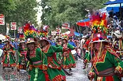 Danseuses de Tinku en costume traditionnel, durant une procession en Bolivie, photo annoncée dans la légende initiale comme prise au Carnaval d’Oruro (si ce n'est la présence des arbres, peu probable à 3 710 m, l'altitude d'Oruro).