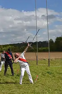 Photo montrant un homme habillé en blanc visant le ciel avec un arc.