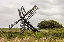 Les ailes d'un moulin se dressent hors du sol vers le ciel.