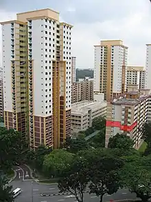 La photographie montre des immeubles d'habitation. Deux d'entre eux, au centre et à gauche, font 26 étages ; les autres sont plus petits. Un des appartements d'un immeuble sur la droite est coloré en rouge sur l'image pour être mis en avant.